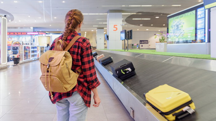A traveller waiting beside an airport baggage carousel as suitcases move past at arrivals.