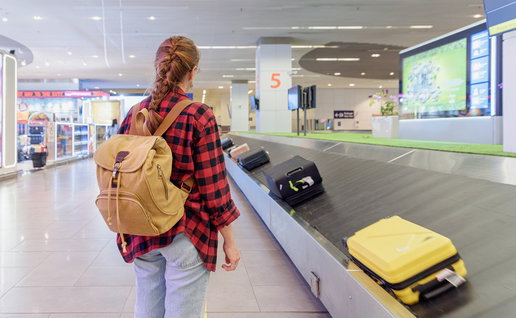A traveller waiting beside an airport baggage carousel as suitcases move past at arrivals.