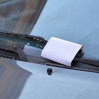A piece of paper tucked under a car windscreen wiper, illustrating a distraction tactic sometimes linked to vehicle theft warnings.