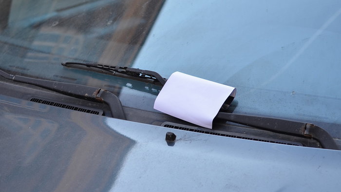 A piece of paper tucked under a car windscreen wiper, illustrating a distraction tactic sometimes linked to vehicle theft warnings.