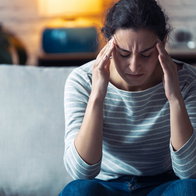 Shot of young woman with headache sitting on the sofa in the living room at home.