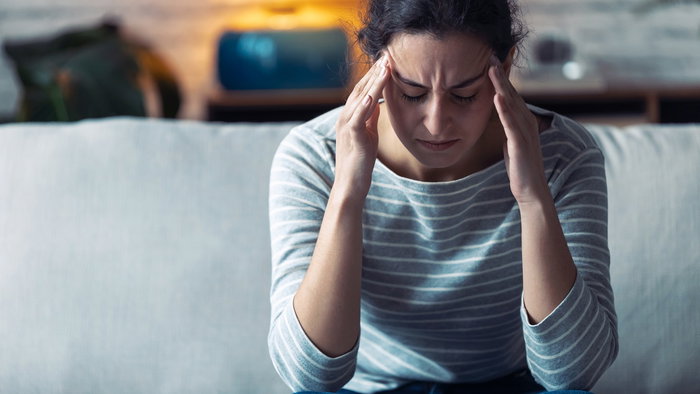 Shot of young woman with headache sitting on the sofa in the living room at home.