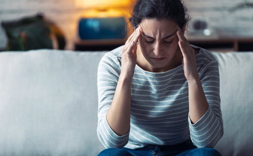 Shot of young woman with headache sitting on the sofa in the living room at home.