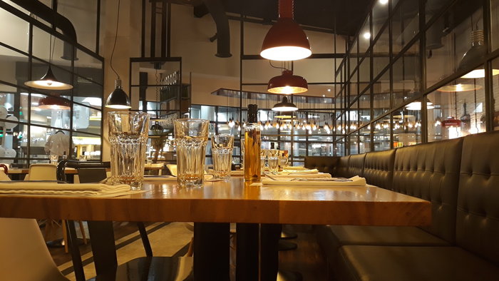Interior of a modern restaurant in Spain with visible ceiling ventilation ducts and dining tables prepared for customers.