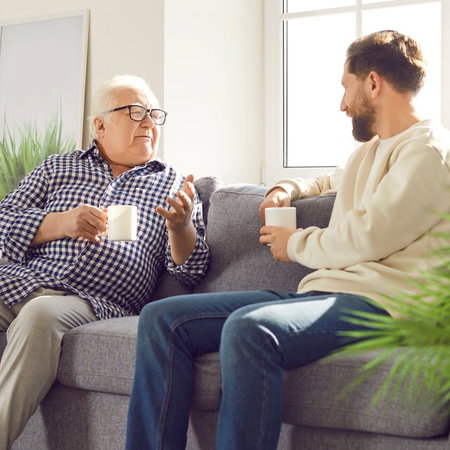 Young man talking to an older parent on a sofa at home in Spain