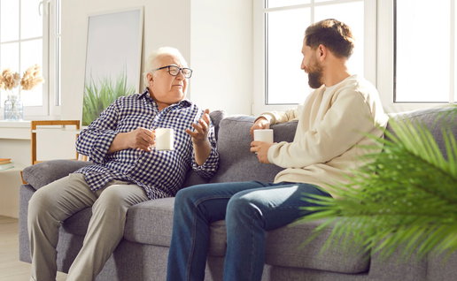 Young man talking to an older parent on a sofa at home in Spain
