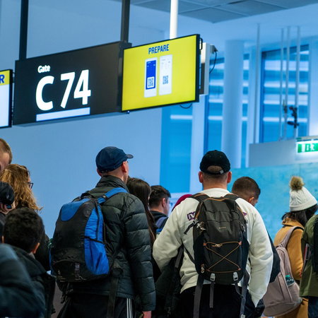 Passengers queue at a Ryanair boarding gate with cabin bags and backpacks before departure.