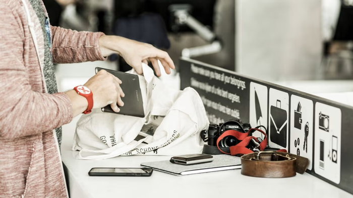 Passengers remove electronic devices and personal items from hand luggage during an airport security screening process.