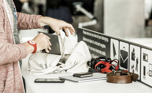 Passengers remove electronic devices and personal items from hand luggage during an airport security screening process.