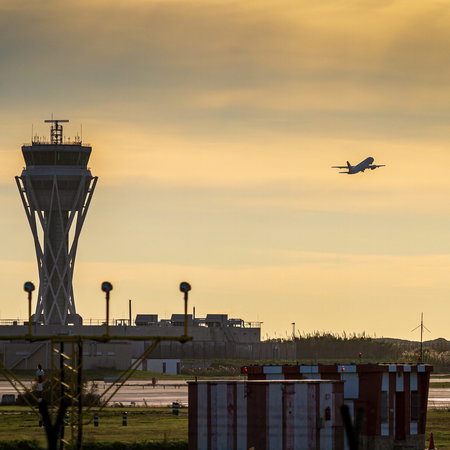 Sunset at an airport with air-traffic control tower and a plane taking off