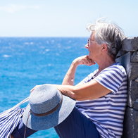Smiling senior woman in striped t-shirt sitting by the sea looking at horizon over water.