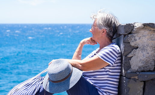 Smiling senior woman in striped t-shirt sitting by the sea looking at horizon over water.