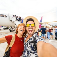 A young couple posing for a selfie in front on a plane.