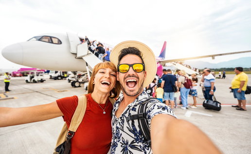 A young couple posing for a selfie in front on a plane.