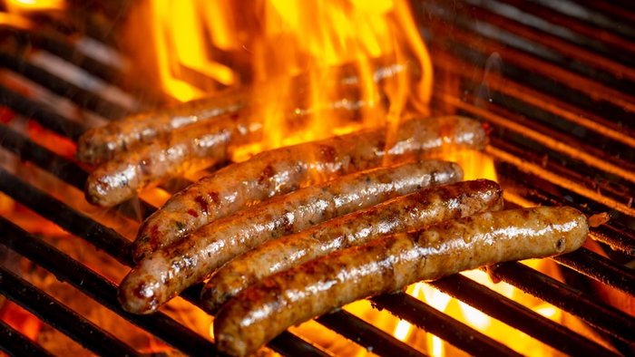 Grilling sausages on the grill with flames and smoke.