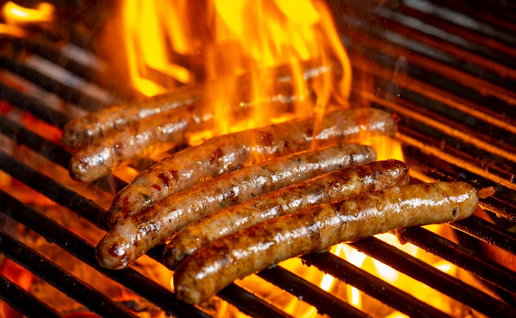 Grilling sausages on the grill with flames and smoke.