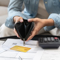 Person opening an empty wallet with a calculator and expenses on the table