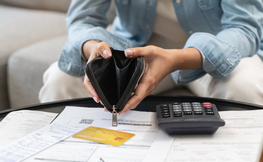 Person opening an empty wallet with a calculator and expenses on the table