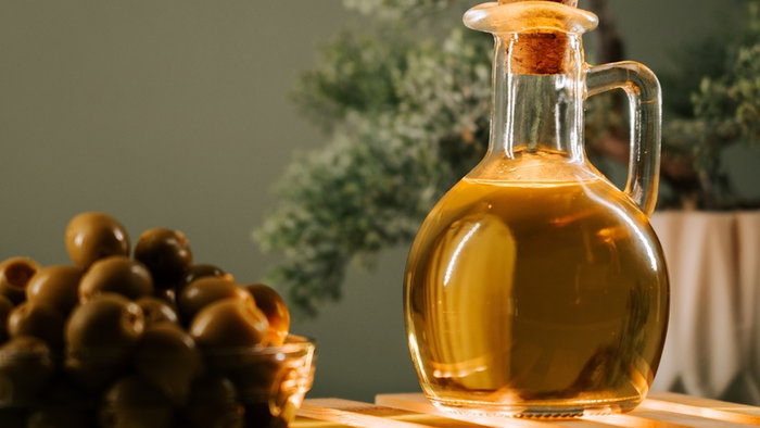 Olive oil in a glass bottle beside a bowl of olives on a wooden surface