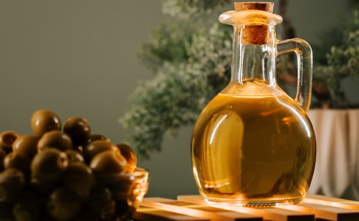 Olive oil in a glass bottle beside a bowl of olives on a wooden surface