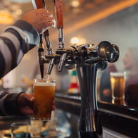 Bartender's hands filling a pint glass with fresh beer from a tap at a busy pub counter, serving drinks