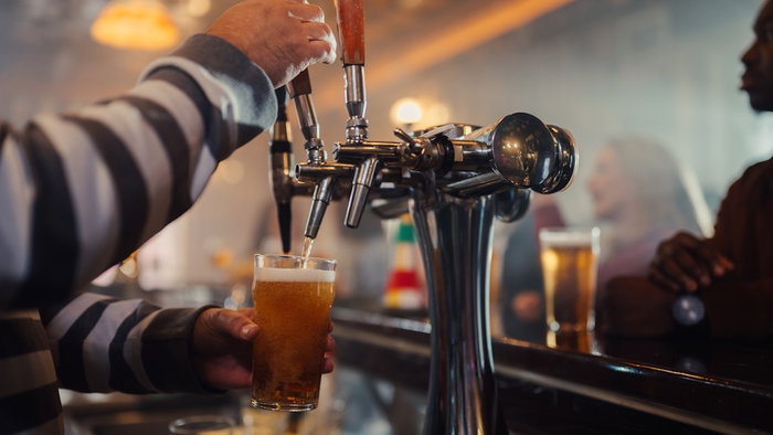 Bartender's hands filling a pint glass with fresh beer from a tap at a busy pub counter, serving drinks