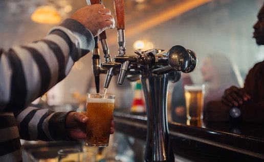 Bartender's hands filling a pint glass with fresh beer from a tap at a busy pub counter, serving drinks