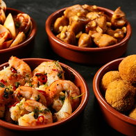 Four round ceramic red bowls of Spanish appetizers knowns as tapas with seafood, nuts and sauces
