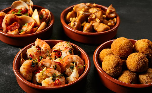 Four round ceramic red bowls of Spanish appetizers knowns as tapas with seafood, nuts and sauces