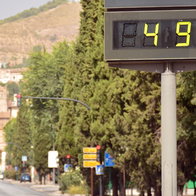 A digital street thermometer in a Spanish city displaying an extreme temperature of 49°C during a summer heatwave, with cars and buildings in the background.