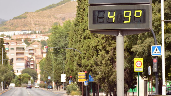 A digital street thermometer in a Spanish city displaying an extreme temperature of 49°C during a summer heatwave, with cars and buildings in the background.