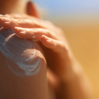 Person applying sunscreen on their shoulder at the beach during summer