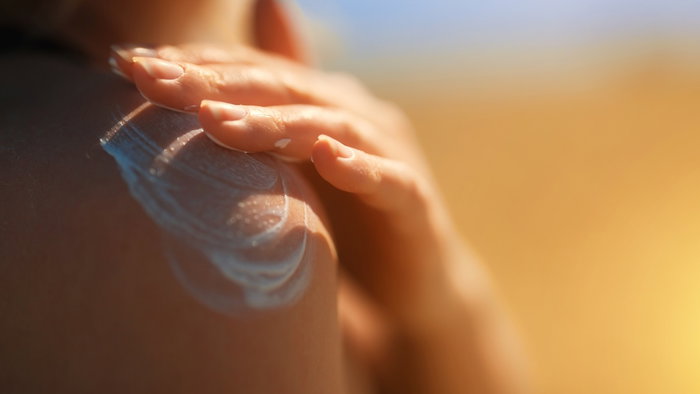 Person applying sunscreen on their shoulder at the beach during summer