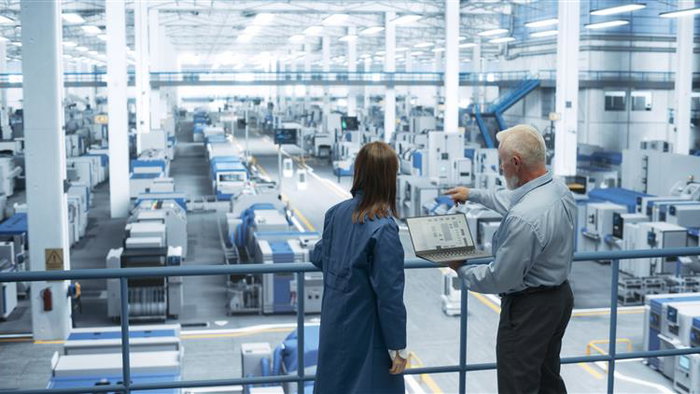 Two engineers standing on a platform looking out at floor with machinery