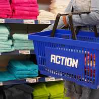 Person carries an Action shopping basket while browsing through products in a supermarket aisle.