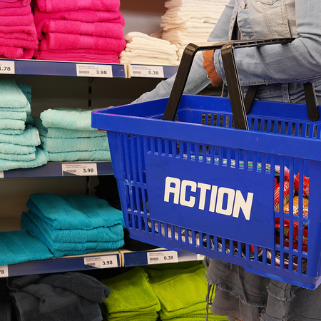 Person carries an Action shopping basket while browsing through products in a supermarket aisle.