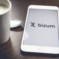A smartphone displaying the Bizum app logo beside a coffee cup, illustrating digital payments and money transfers in Spain.