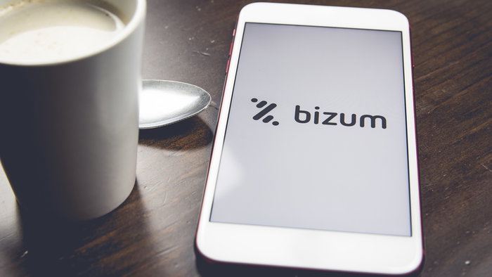 A smartphone displaying the Bizum app logo beside a coffee cup, illustrating digital payments and money transfers in Spain.