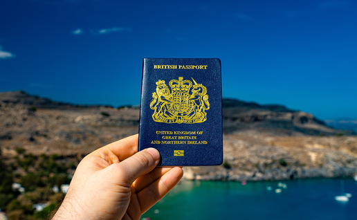 British passport held up against a sunny beach coast.