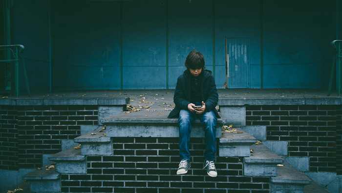 Child sat alone staring at phone in hand