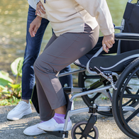Elderly woman gets out of wheelchair with help from carer.
