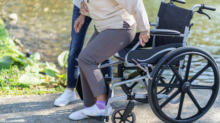 Elderly woman gets out of wheelchair with help from carer.