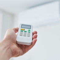 View of a hand holding a remote control for a air-conditioning unit