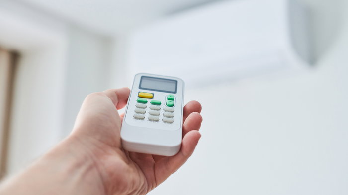 View of a hand holding a remote control for a air-conditioning unit