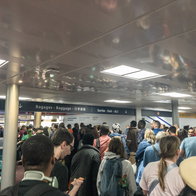 Crowds of passengers waiting in a packed airport terminal as long queues create delays near border control and departure areas.