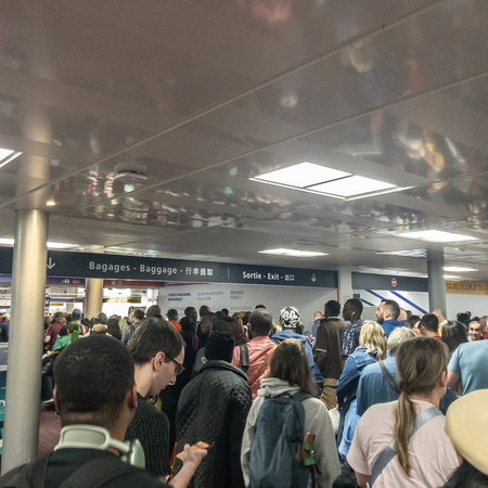 Crowds of passengers waiting in a packed airport terminal as long queues create delays near border control and departure areas.