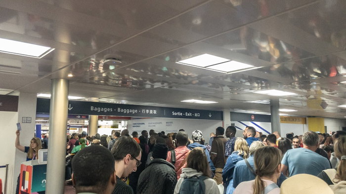 Crowds of passengers waiting in a packed airport terminal as long queues create delays near border control and departure areas.