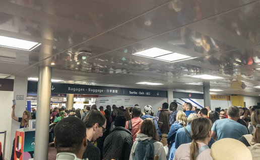 Crowds of passengers waiting in a packed airport terminal as long queues create delays near border control and departure areas.