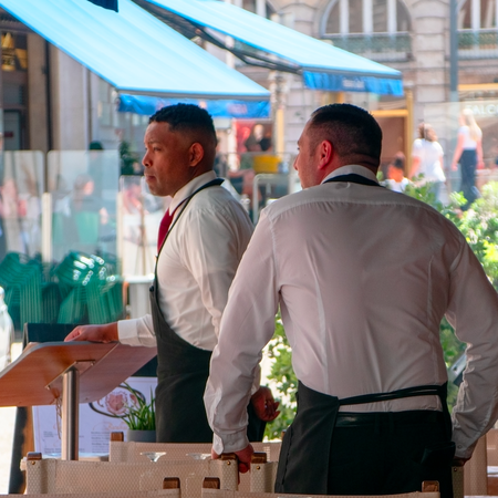 Two waiters in the terrace of a restaurant looking to attract clients