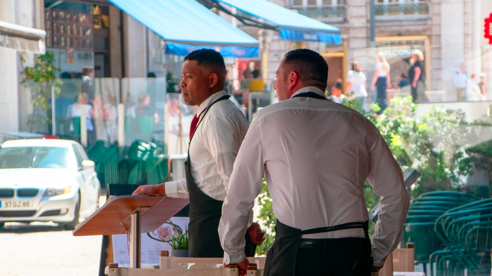 Two waiters in the terrace of a restaurant looking to attract clients